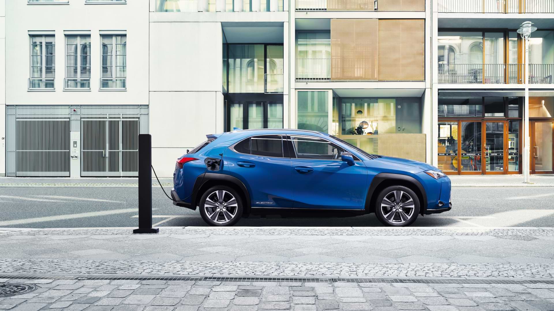 A blue UX 300e sits parked in the daylight, being charged.